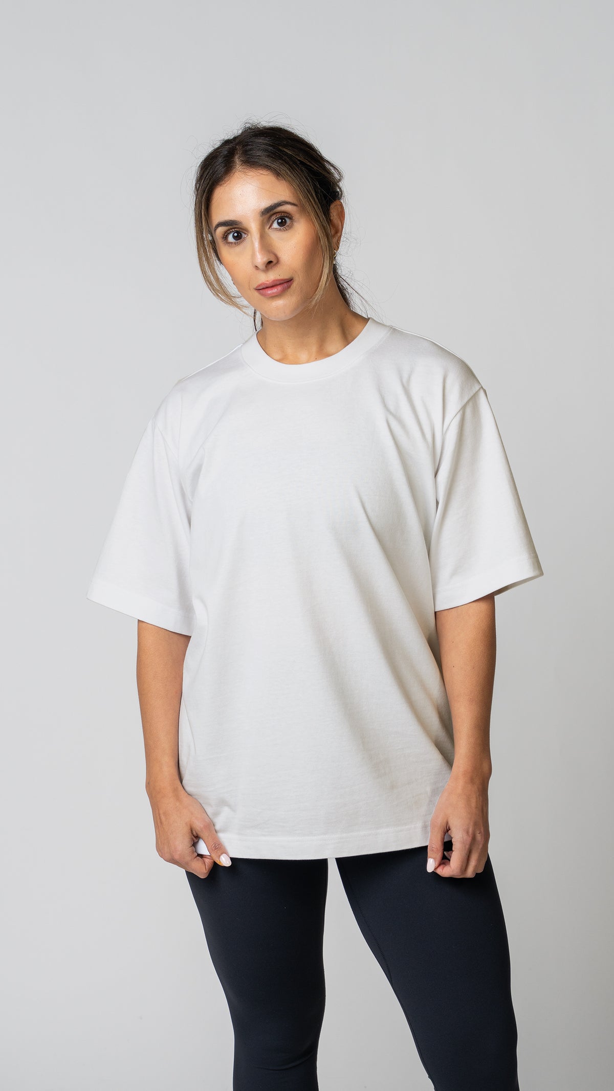 Woman wearing a plain white t-shirt and dark tights on a light gray background