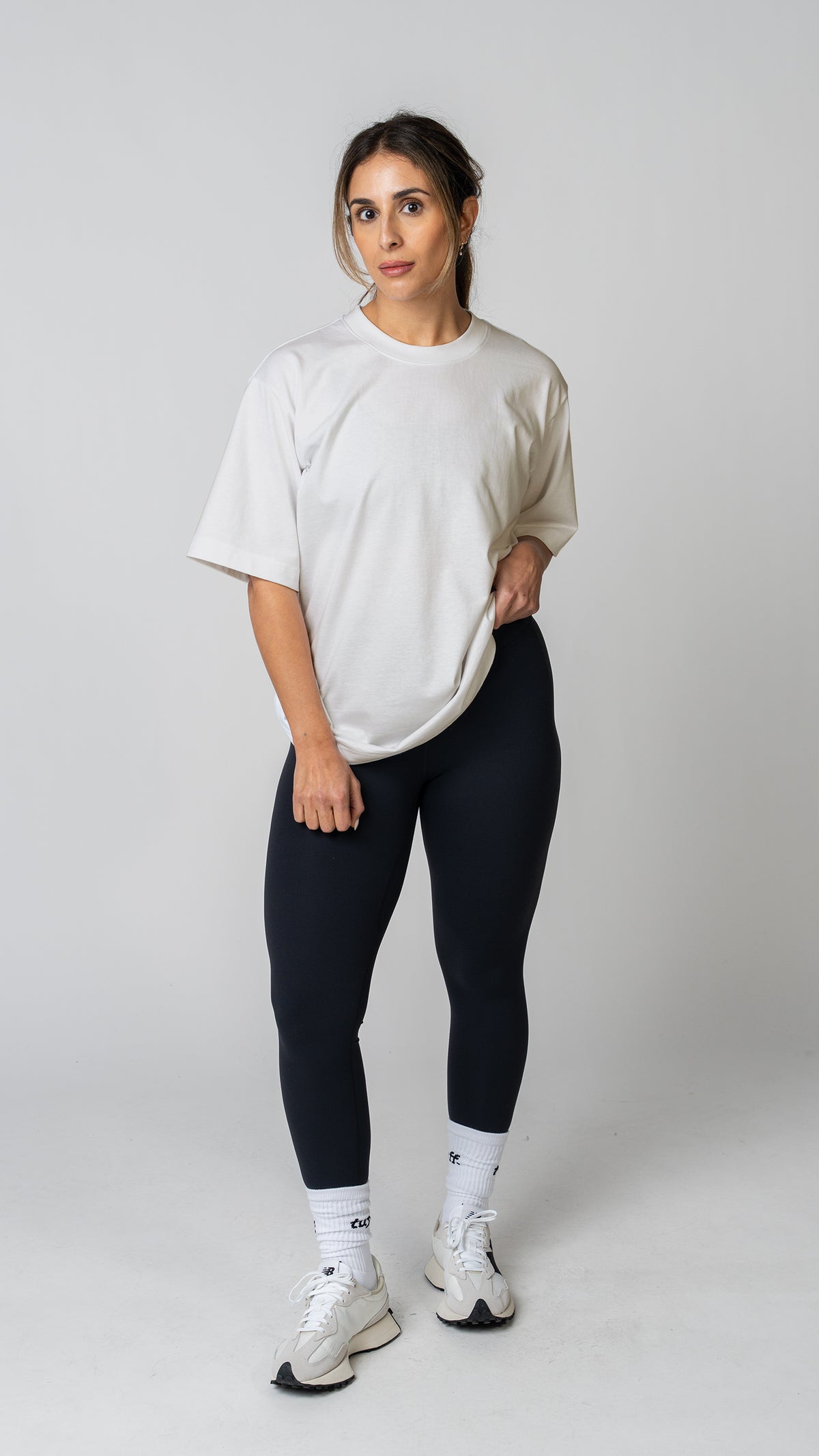 Woman wearing a plain white t-shirt and dark tights on a light gray background