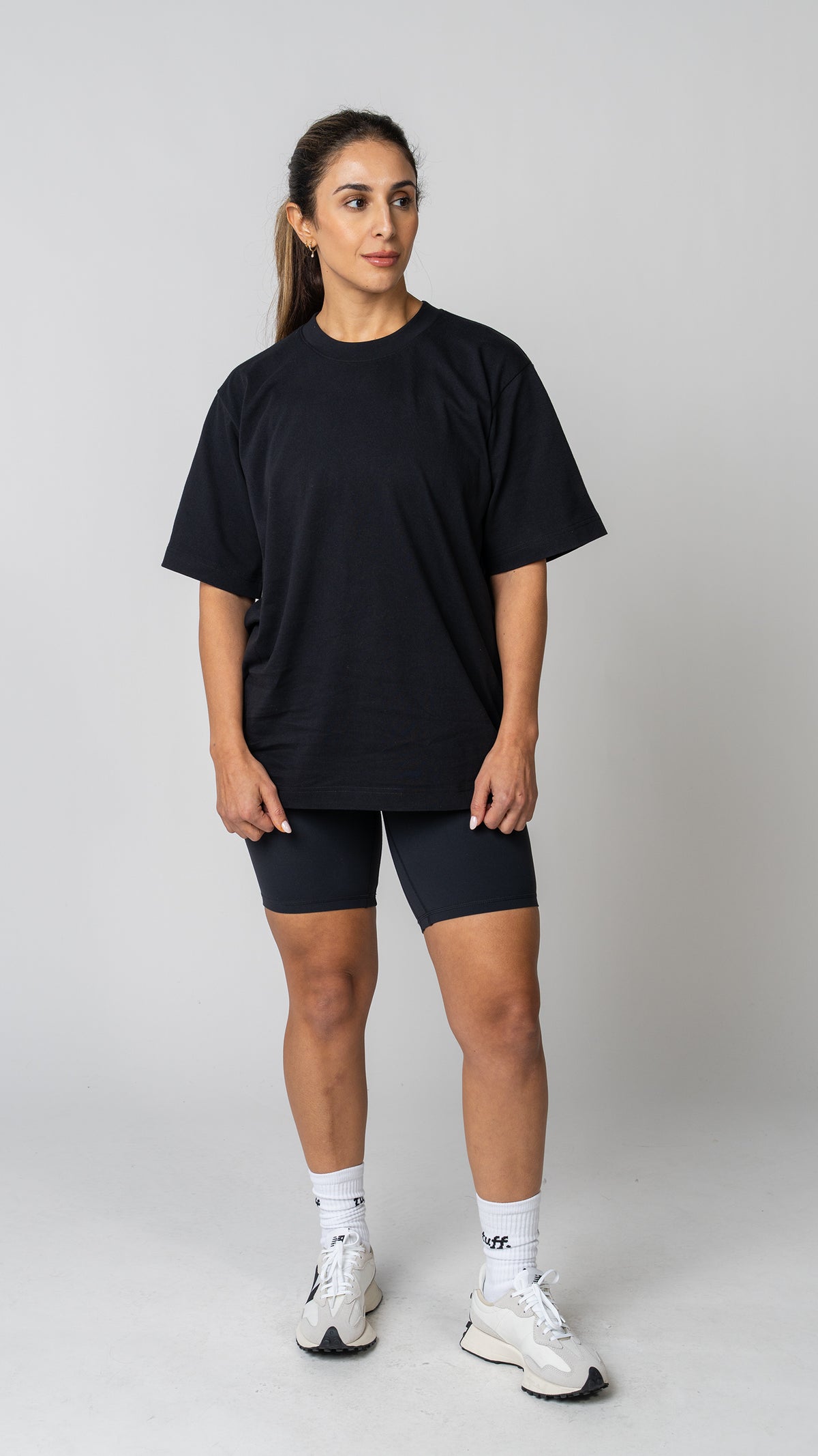 Woman wearing a plain white t-shirt and dark tights on a light gray background