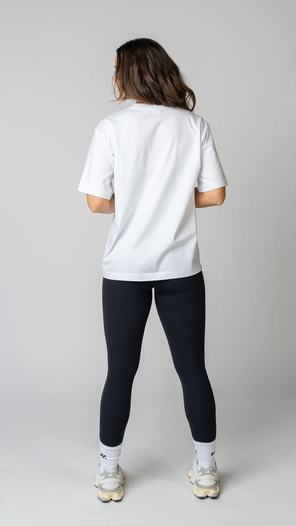 women wearing a white oversized tee with black leggings. back side view. 